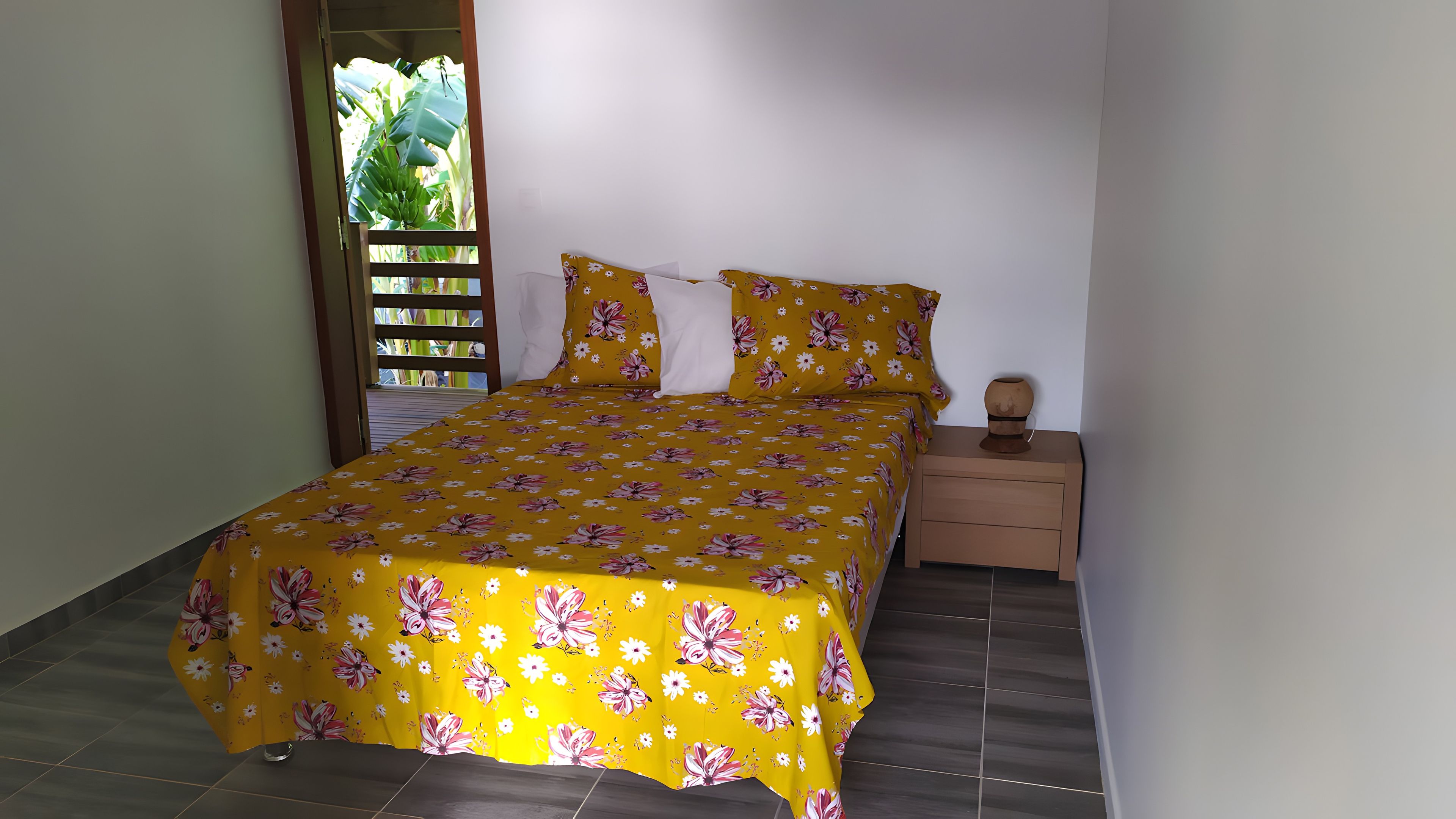 Een kamer met een bed, een nachtkastje en een raam met uitzicht op groen.