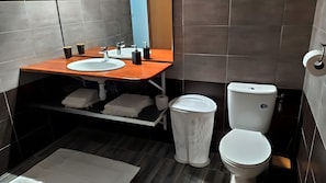 Een moderne badkamer met een houten wastafelmeubel, een witte wastafel, een toilet en een witte wasmand.