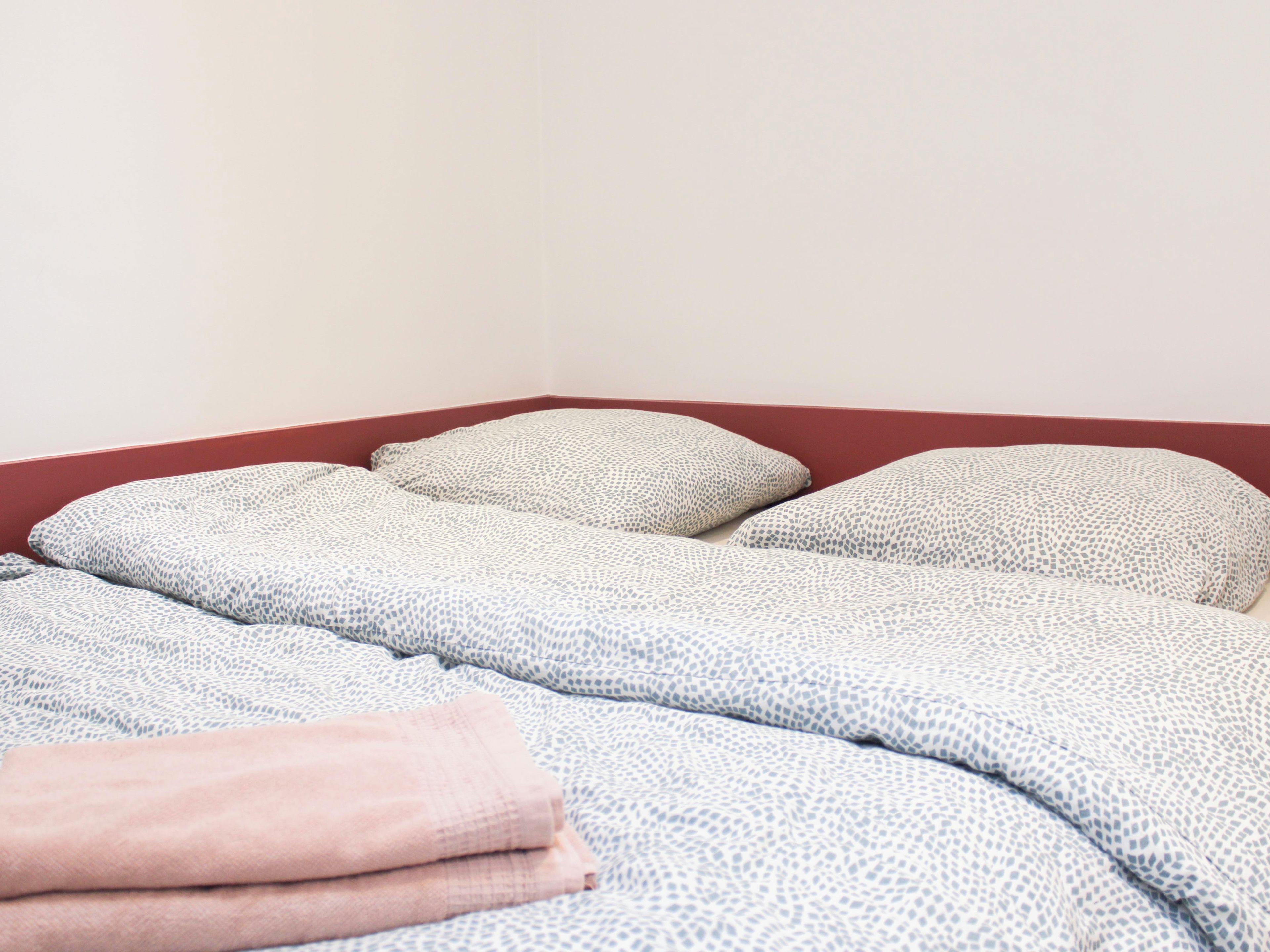 Ein Bett mit einem gemusterten Überwurf und Kissen, einer gefalteten Decke und einem roten Kopfteil.