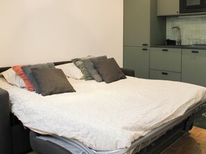 A bed with a white duvet and multiple pillows, a small bedside table, and a view of a kitchen area with cabinets and a sink. - One-bedroom apartment for 4 guests in Paris 9 (Paris)