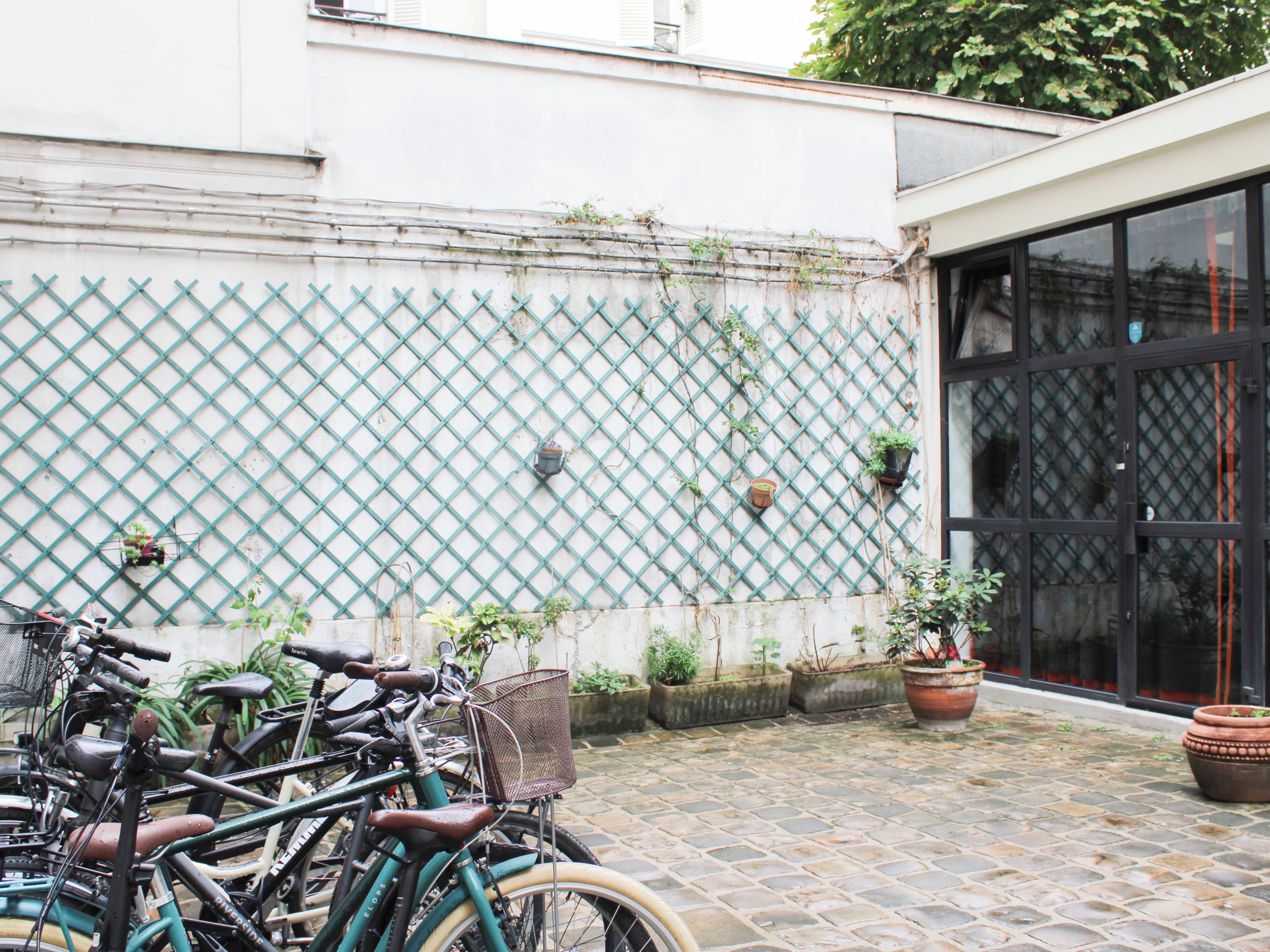 Un patio con bicicletas estacionadas frente a una pared con diseño de celosía, plantas en macetas y un ventanal grande.