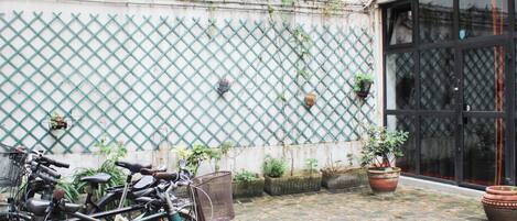 A courtyard with bicycles parked against a wall with a lattice design, potted plants, and a large window.
