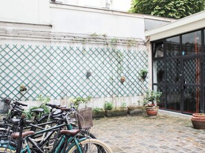 A courtyard with bicycles parked against a wall with a lattice design, potted plants, and a large window. - One-bedroom apartment for 4 guests in Paris 9 (Paris)