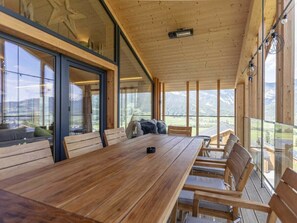 A spacious room with a long wooden table and chairs, large windows offering a view of the outdoors, and a ceiling with wooden beams. - One-bedroom Cabin (Haus)
