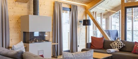Ein gemütliches Wohnzimmer mit Kamin, Holzwänden und großen Fenstern.