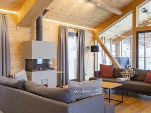 Een gezellige woonkamer met een open haard, houten wanden en grote ramen.
