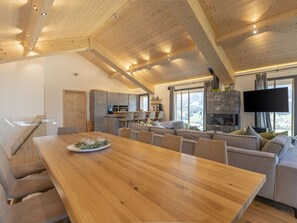 A modern interior with a wooden dining table, a sofa set, a kitchen area, and a stone fireplace. - One-bedroom Cabin (Haus)