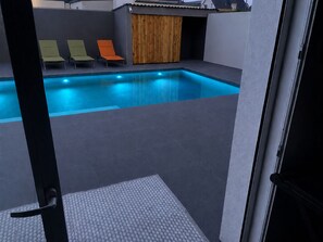 Una piscina con tres sillas de descanso, una puerta de madera y suelo de baldosas.