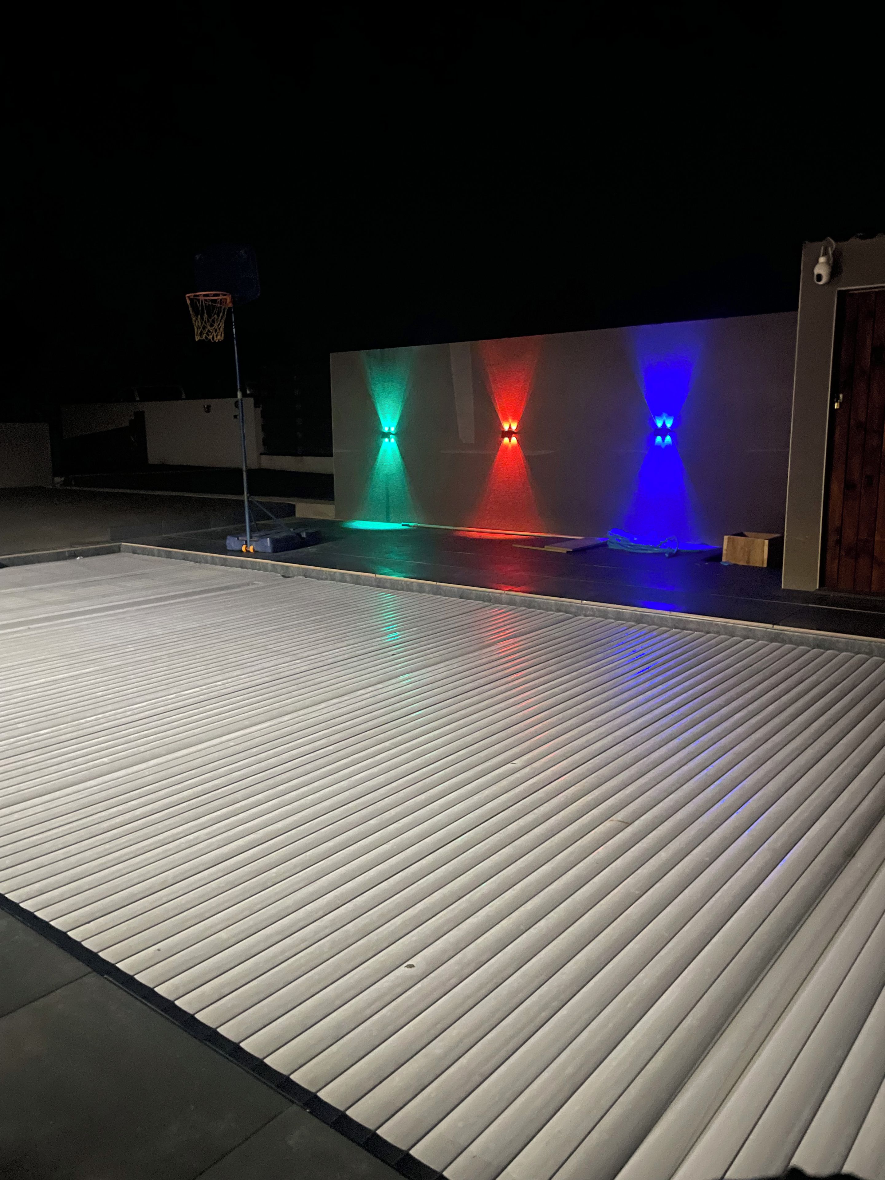 A rooftop with a basketball hoop and a flat surface with colored lights.