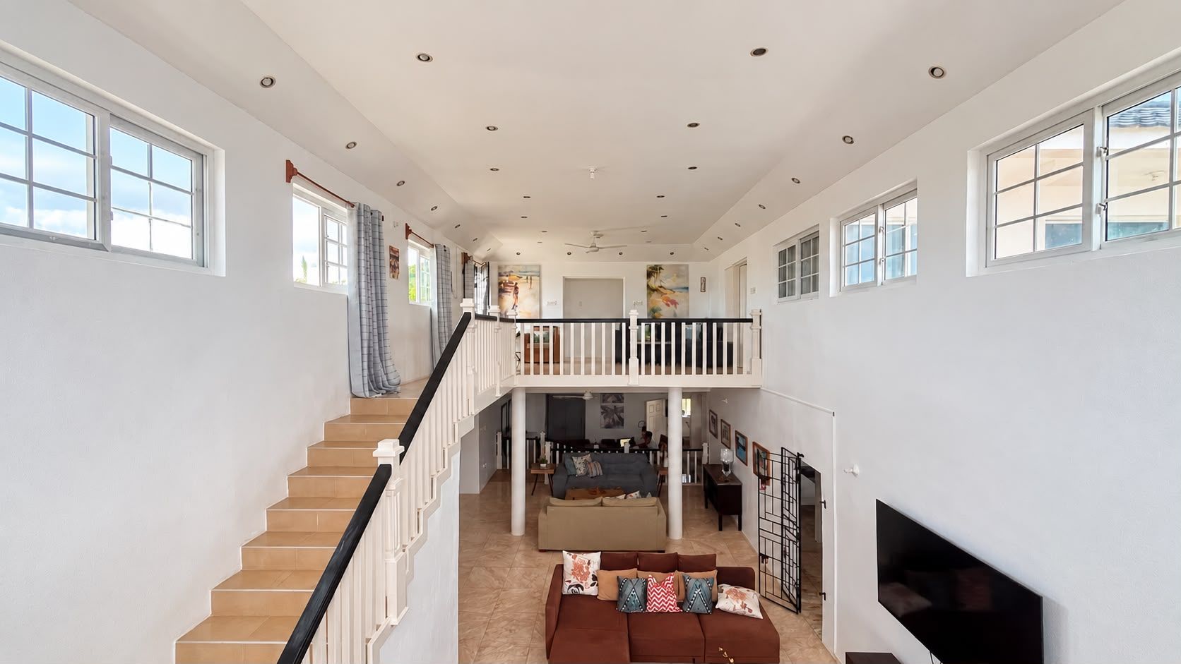Un interior amplio con una escalera que lleva a un balcón, una sala de estar con un sof á y un televisor de pantalla plana montado en la pared.