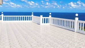 Ein weißer Balkon mit Fliesenboden und weißen Geländern, mit Blick auf einen klaren, blauen Himmel und ruhiges Meer.