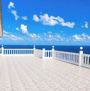 A white balcony with a tiled floor and white balustrades, overlooking a clear blue sky and a calm sea. - Da Villa Juanita (Hordley)