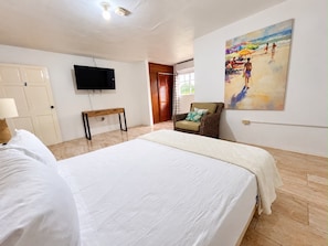 A hotel room with a bed, a television, a chair, and a painting on the wall. - Da Villa Juanita (Hordley)
