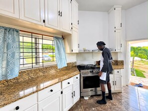 Una cocina con gabinetes blancos, encimera de granito y una persona cocinando.