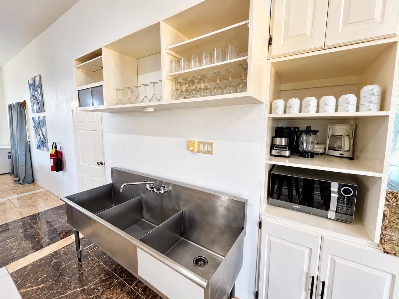 Una cocina moderna con un lavamanos de acero inoxidable, muebles blancos y una cafetera.