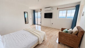 Un dormitorio con cama, televisor, ventana con cortinas y vista al mar.