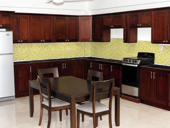 Una cocina con armarios de madera oscura, salpicadero de azulejos, estufa y mesa de comedor con sillas.