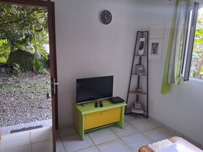 Une pièce avec un téléviseur posé sur un meuble vert et jaune, une horloge au mur et une fenêtre avec des rideaux.