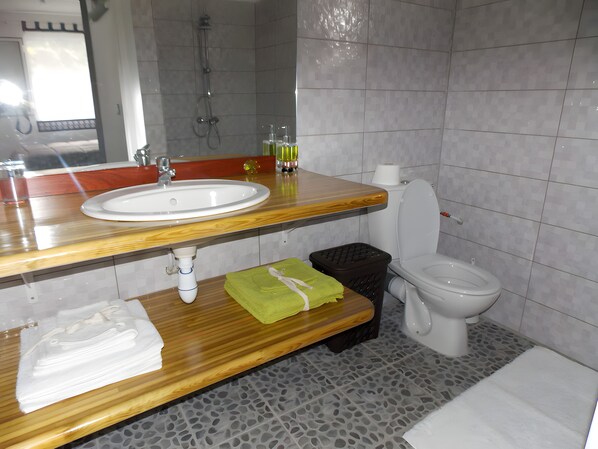 Une salle de bain avec un meuble-lavabo en bois, un lavabo blanc, des toilettes et un espace douche.