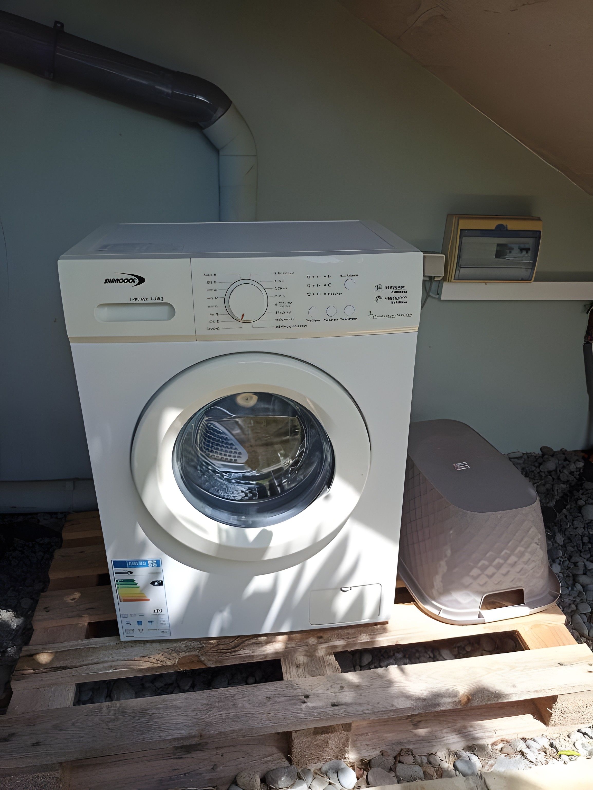 A front-loading washing machine on a wooden pallet, with a control panel and a label indicating it is a Maytag model.