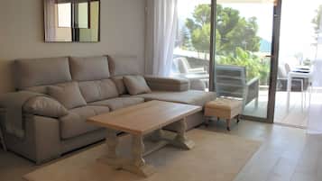 Un salon moderne comprenant un canapé, une table basse et une porte-fenêtre coulissante donnant sur un espace extérieur avec vue sur les arbres.