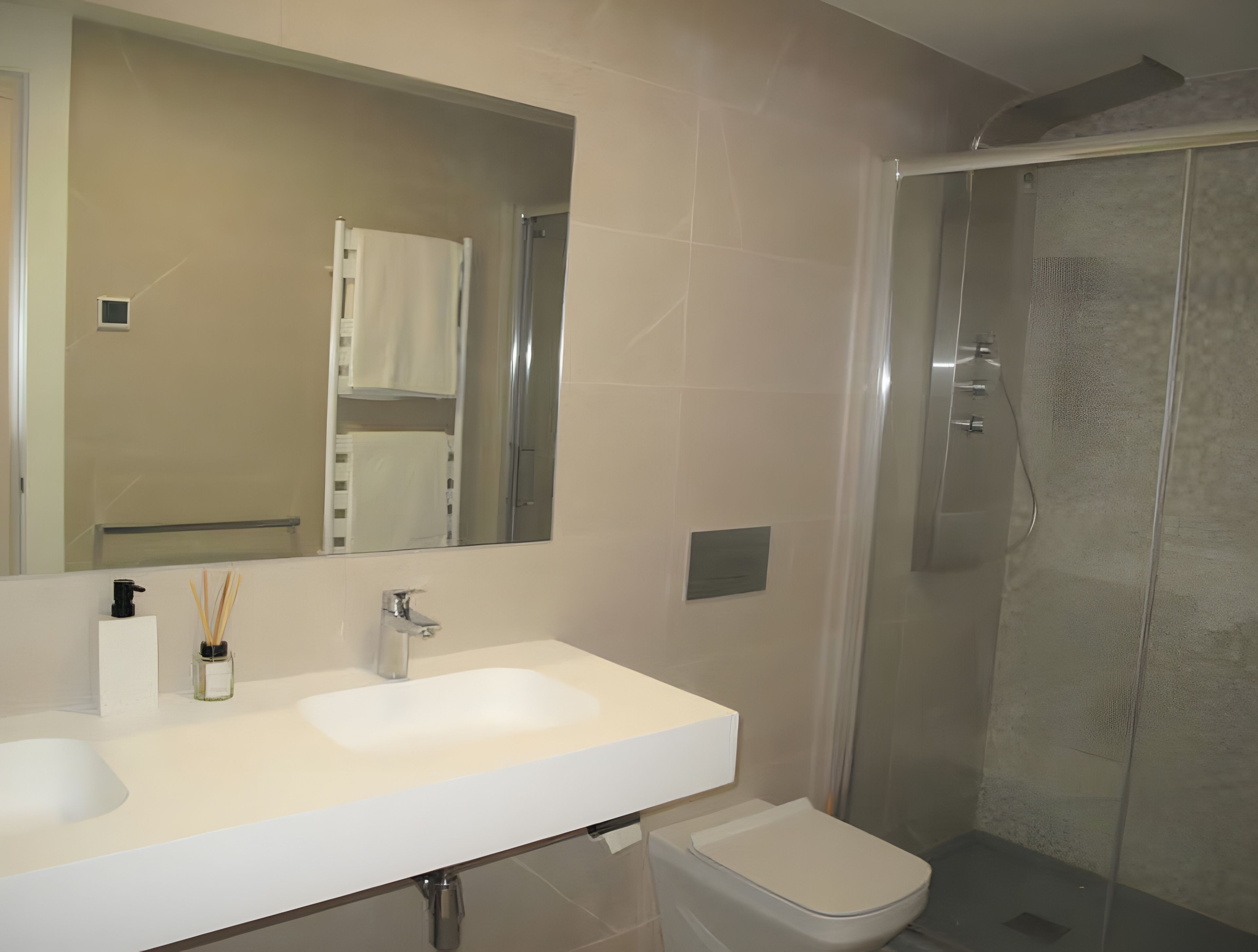Un baño con lavamanos blanco, espejo, inodoro y ducha con cerramiento de vidrio.