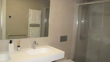 Un baño con lavamanos blanco, espejo, inodoro y ducha con cerramiento de vidrio.