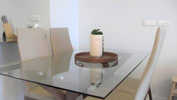 Un comedor moderno con una mesa de vidrio, dos sillas, una planta en maceta y una mesita de madera.