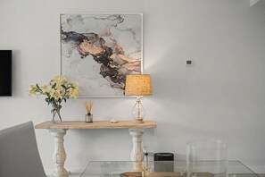Un comedor con una mesa de mármol, un jarrón de flores, una lámpara y una obra de arte en la pared.
