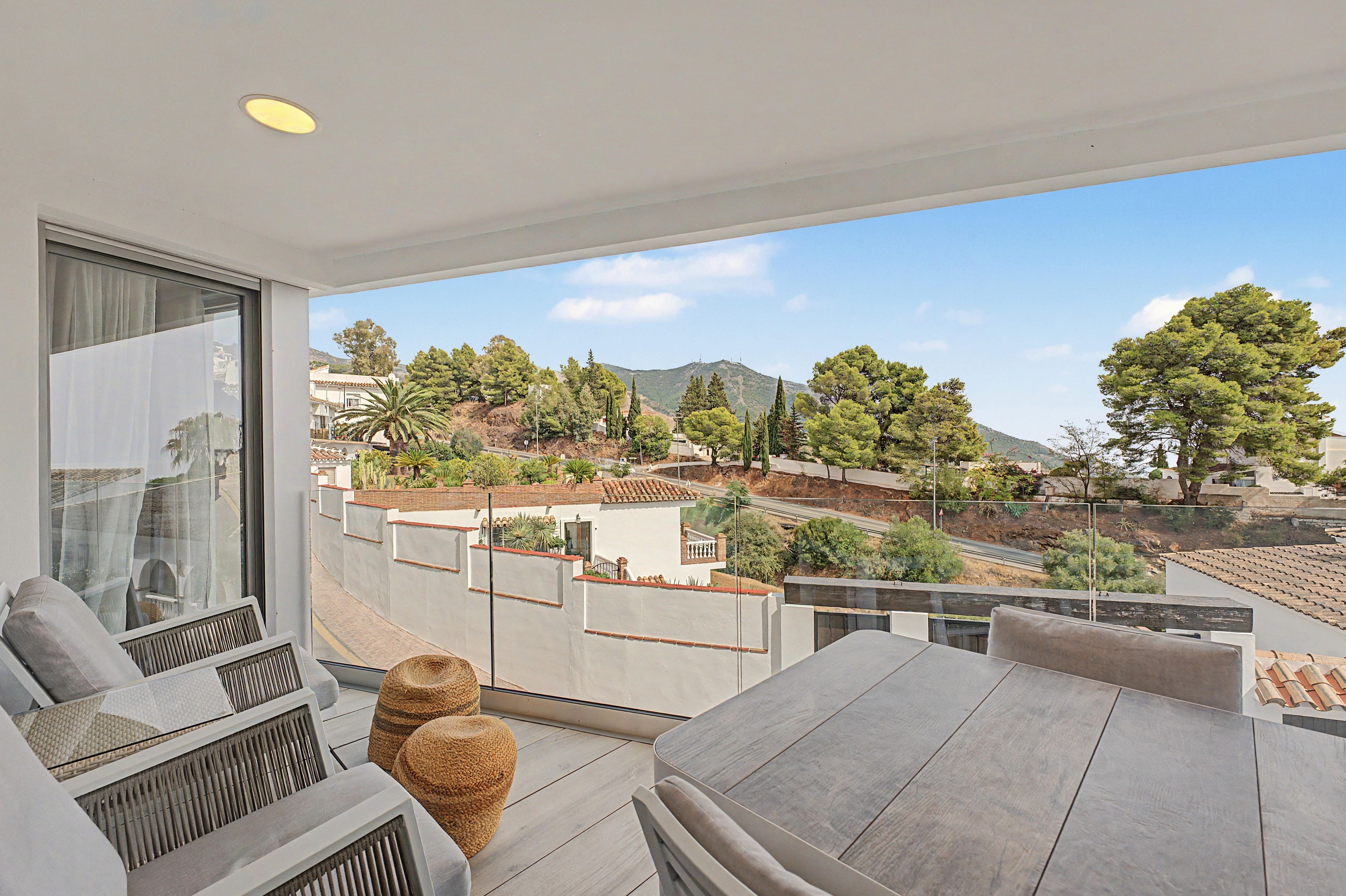 A balcony with a view of a hilly landscape, a table, and chairs.