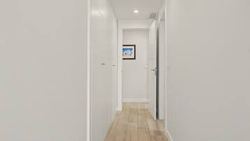 Un corridoio stretto con pareti bianche e pavimento in legno, che conduce a una porta con un quadro incorniciato appeso al muro.