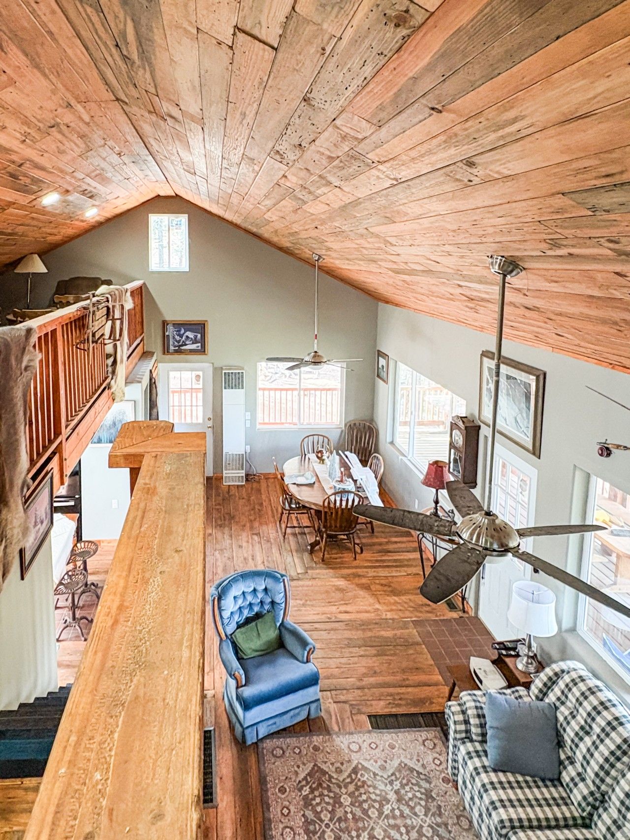 A spacious loft with a high ceiling, wooden beams, a dining area with a table and chairs, a blue armchair, and a checkered sofa.
