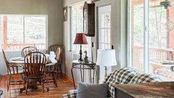 Um quarto aconchegante com teto de madeira, área de jantar com mesa e cadeiras, sofá e uma janela grande.