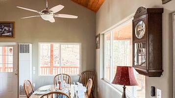 A dining area with a wooden ceiling, a ceiling fan, a dining table with chairs, and a clock on the wall.
