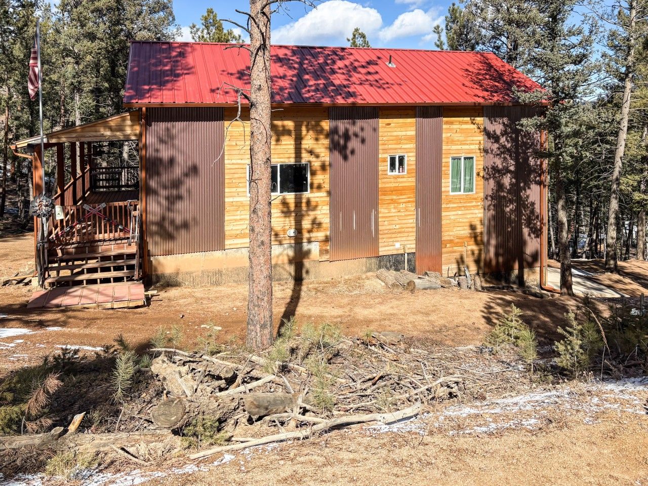 A cabin with a red roof, wooden walls, and a covered porch.