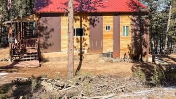 A cabin with a red roof, wooden walls, and a covered porch.