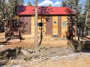 A cabin with a red roof, wooden walls, and a covered porch.