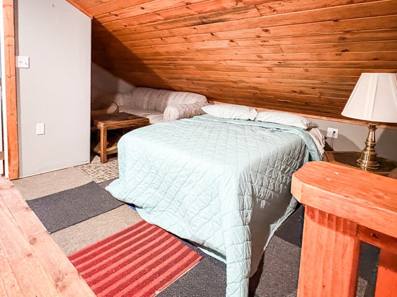 Ein Schlafzimmer mit einem Bett, einem Nachttisch, einer Lampe und einem roten Teppich.