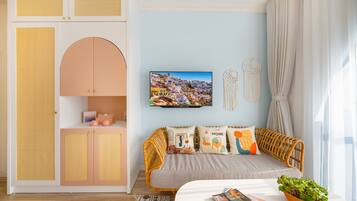 A room with a sofa, a television, a wall-mounted picture, and a decorative macrame piece.