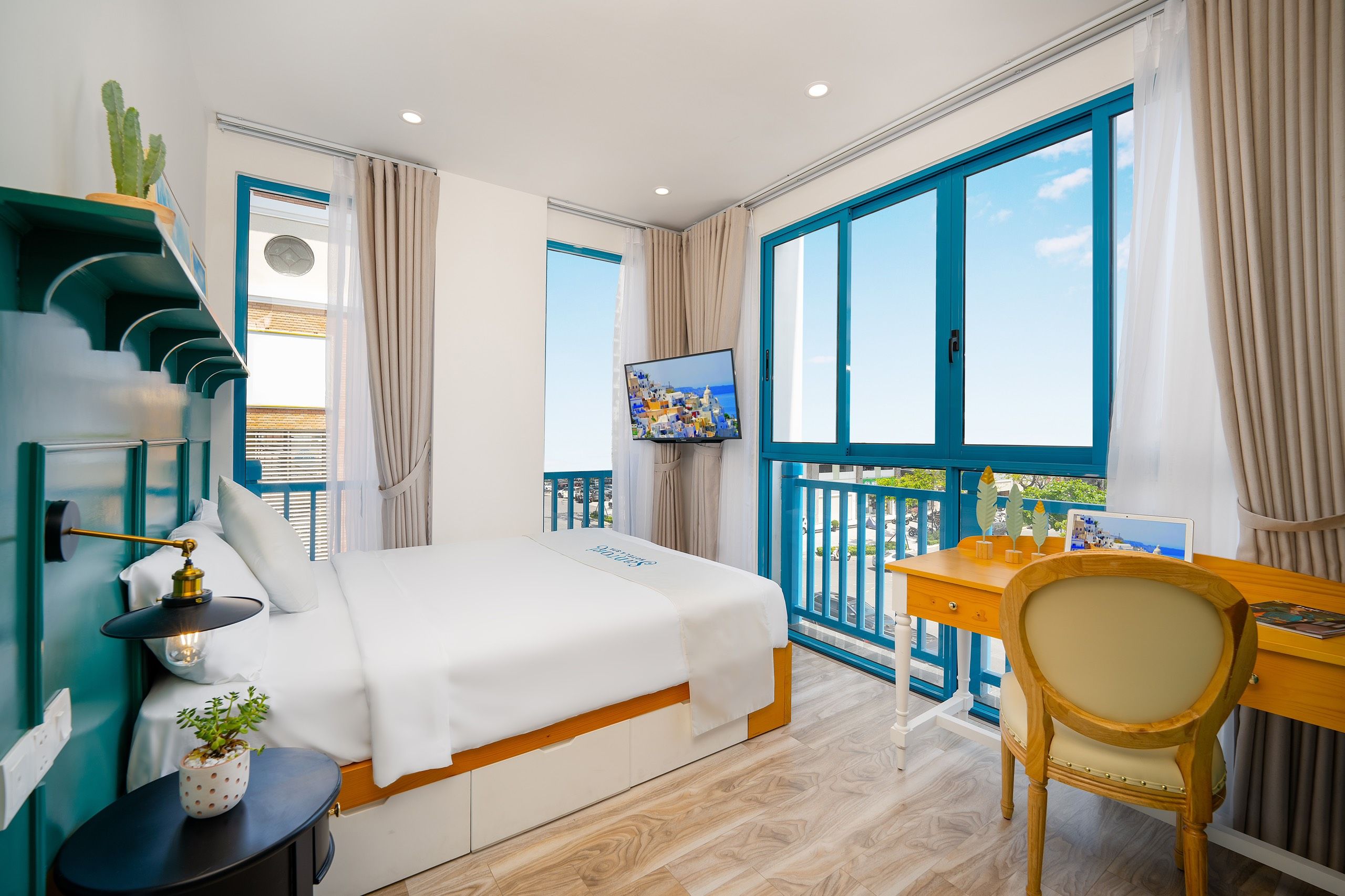 A hotel room with a bed, a desk, a chair, a TV, and a balcony with a view.