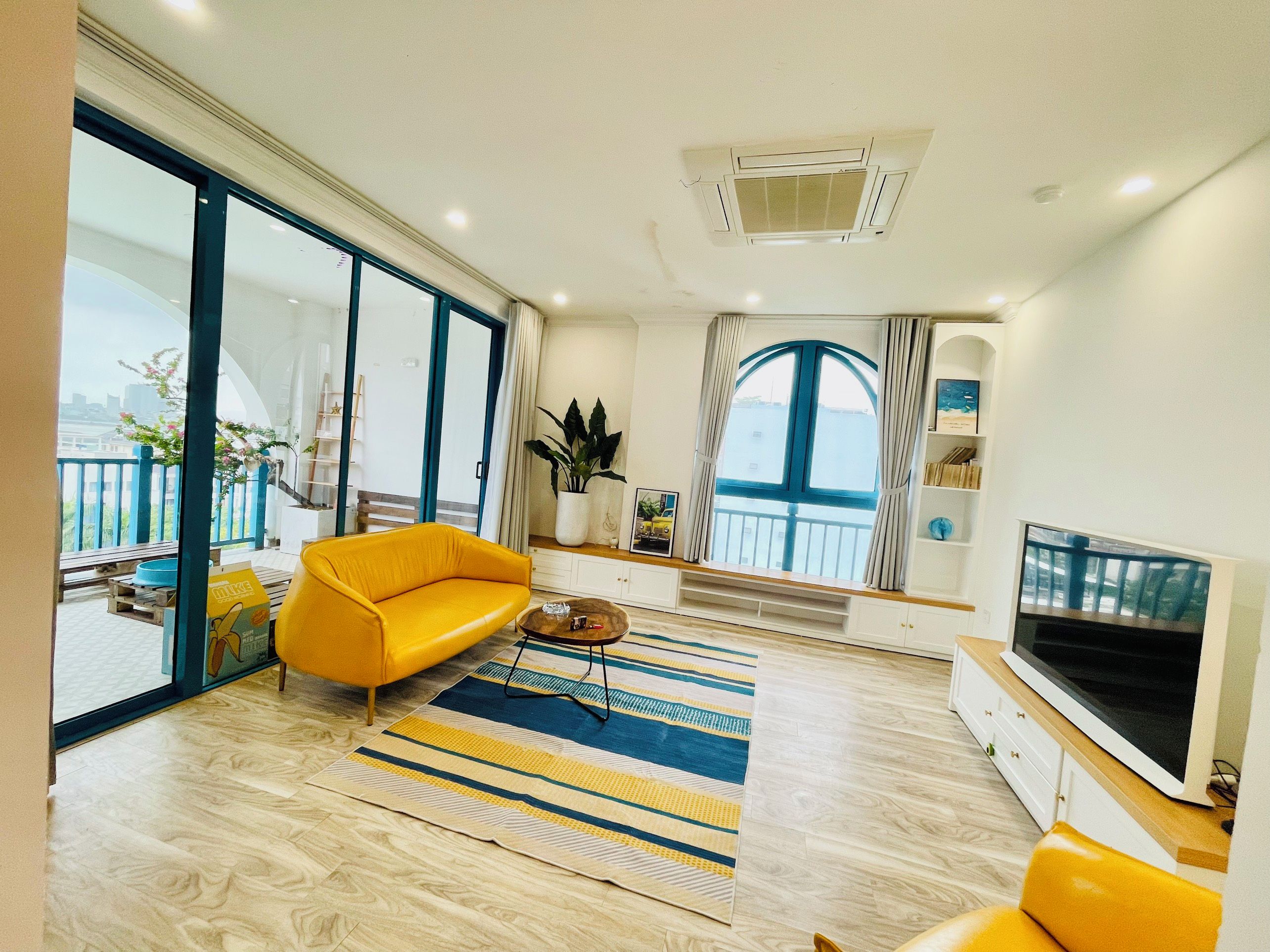 A modern living room with a sofa, a coffee table, a TV, and a large window with a view.