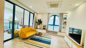 A modern living room with a sofa, a coffee table, a TV, and a large window with a view.