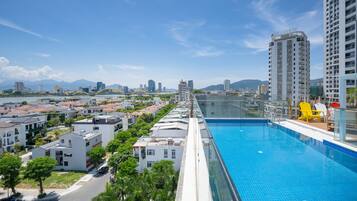 A modern hotel with a rooftop pool, a view of the cityscape, and a bridge in the background.