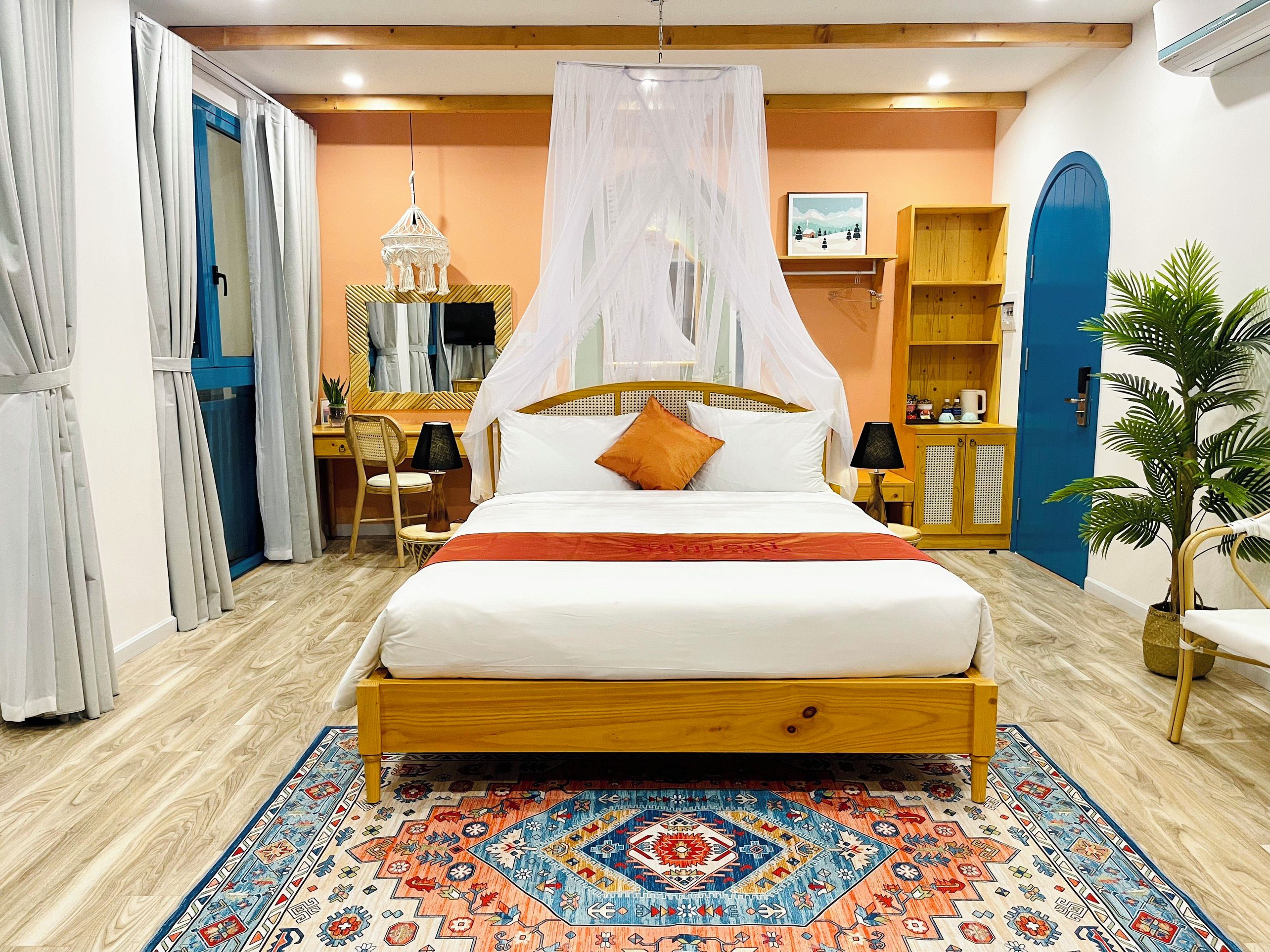 A bedroom with a bed, a desk, a chair, a wardrobe, and a large potted plant.