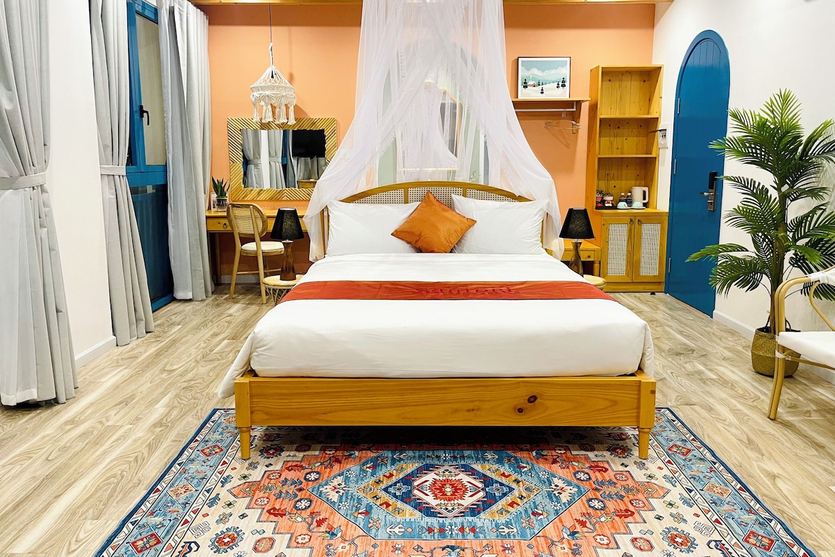 Quarto com cama, escrivaninha, cadeira, guarda-roupa e uma grande planta em vaso.