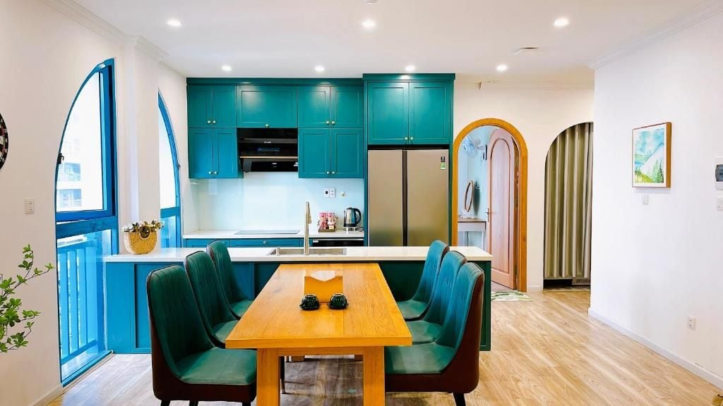 A modern kitchen with teal cabinets, a wooden dining table with chairs, and a refrigerator.