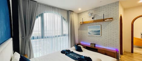 A hotel room with a large bed, a bedside table, a wall-mounted fan, and a window with curtains.