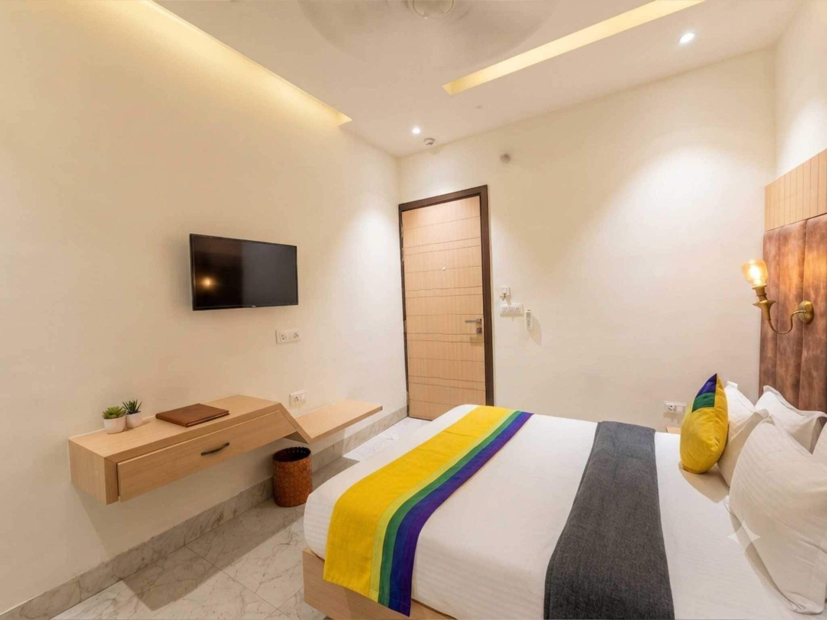 A modern bedroom with a bed, a TV mounted on the wall, a wooden bedside table, and a small plant.