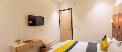 A modern bedroom with a bed, a TV mounted on the wall, a wooden bedside table, and a small plant.
