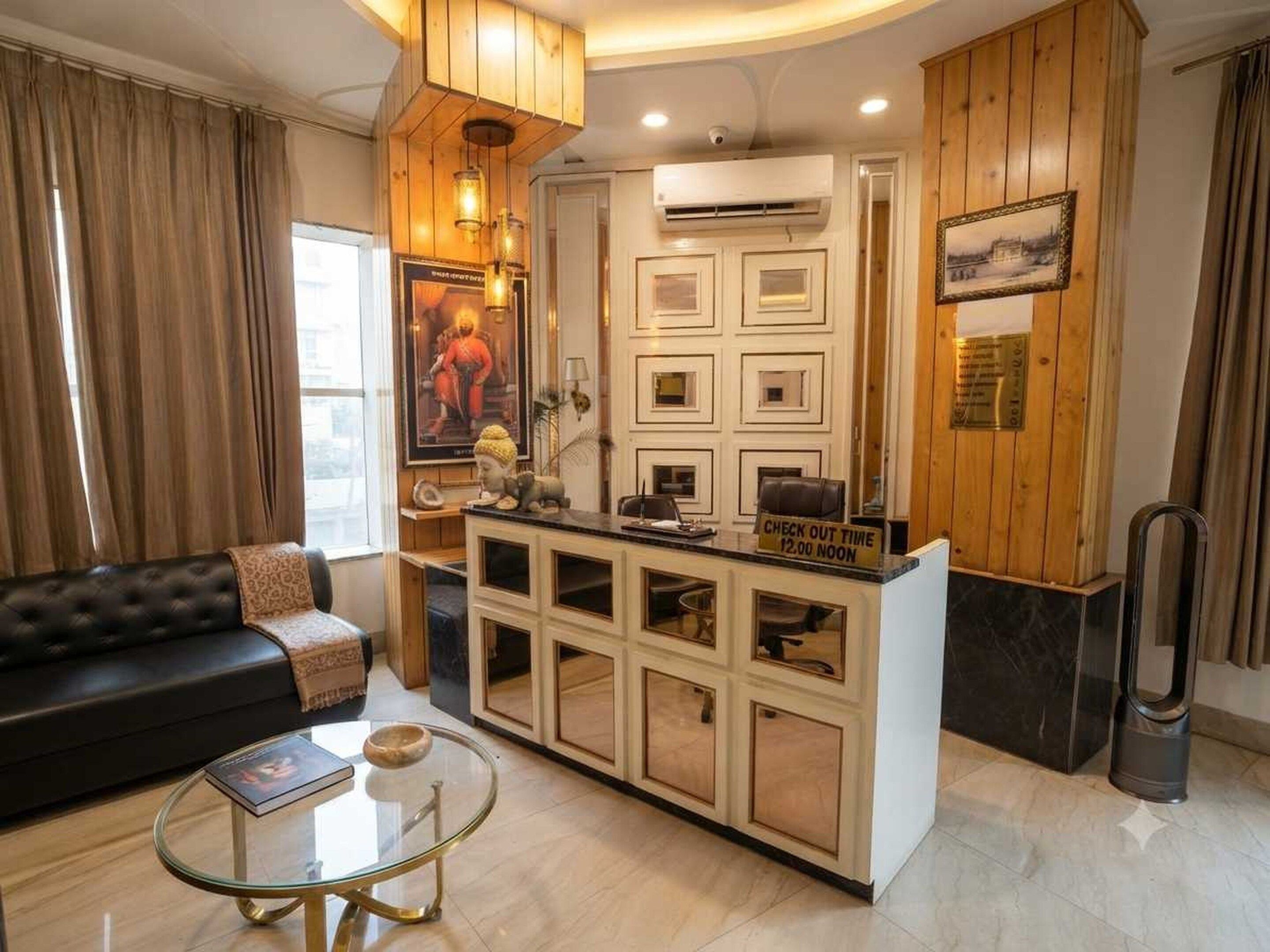 Un hall d’hôtel moderne avec un canapé en cuir noir, une table basse en verre, un comptoir de réception indiquant l’heure limite pour effectuer le départ, et une grande affiche accrochée au mur.